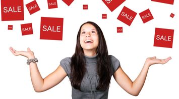 A woman smiling and looking upwards with open hands, surrounded by multiple red 'SALE' signs floating in the air against a white background