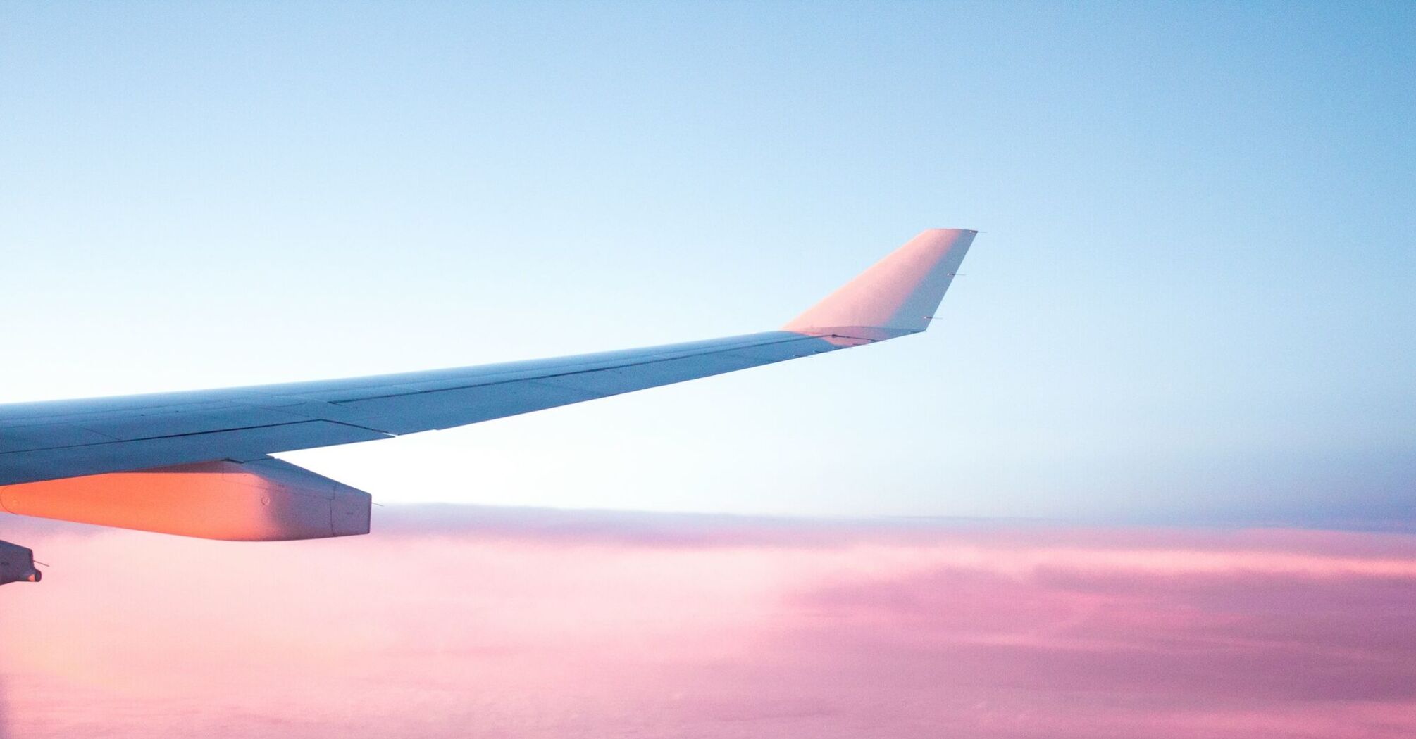 View of an airplane wing against a pink-hued sky during sunset