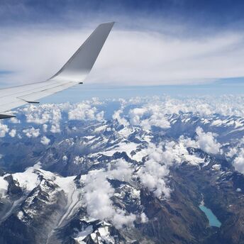 View of majestic snow-capped mountains and clouds from the window of an airplane, with the wing in the foreground
