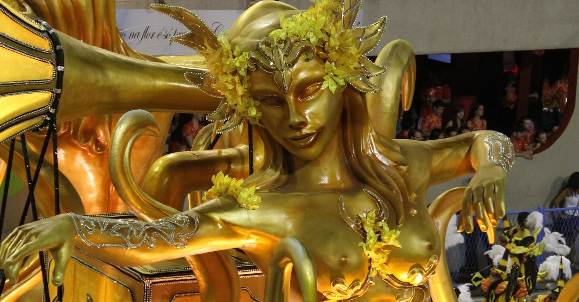 A golden statue of a mythical figure with outstretched arms, adorned with yellow floral decorations