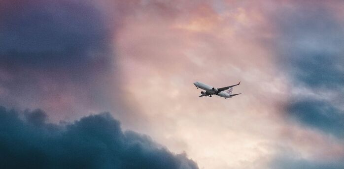 Commercial airplane ascending through a dramatic sky with pink-hued clouds at sunset 