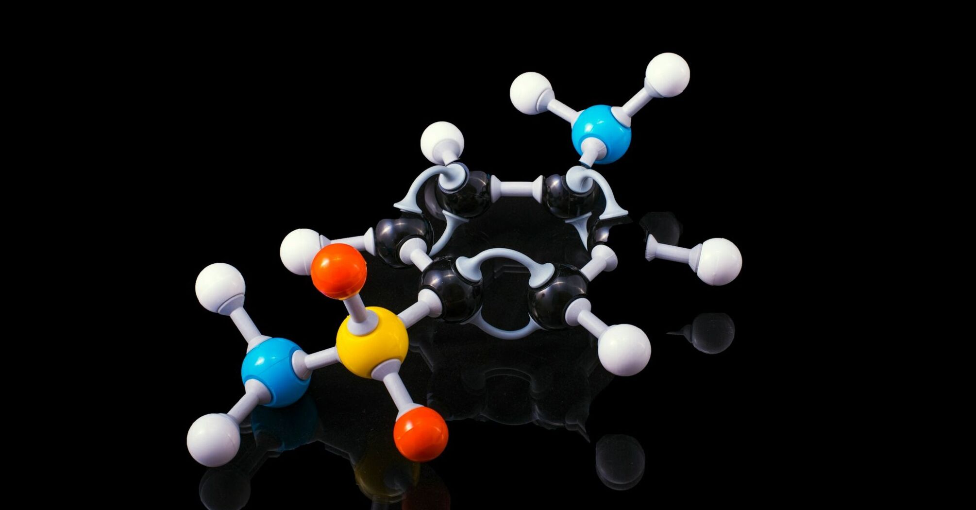 Model of a molecule with colorful balls representing different atoms connected by sticks to illustrate bonds, on a reflective black surface