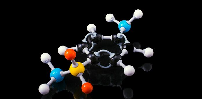 Model of a molecule with colorful balls representing different atoms connected by sticks to illustrate bonds, on a reflective black surface