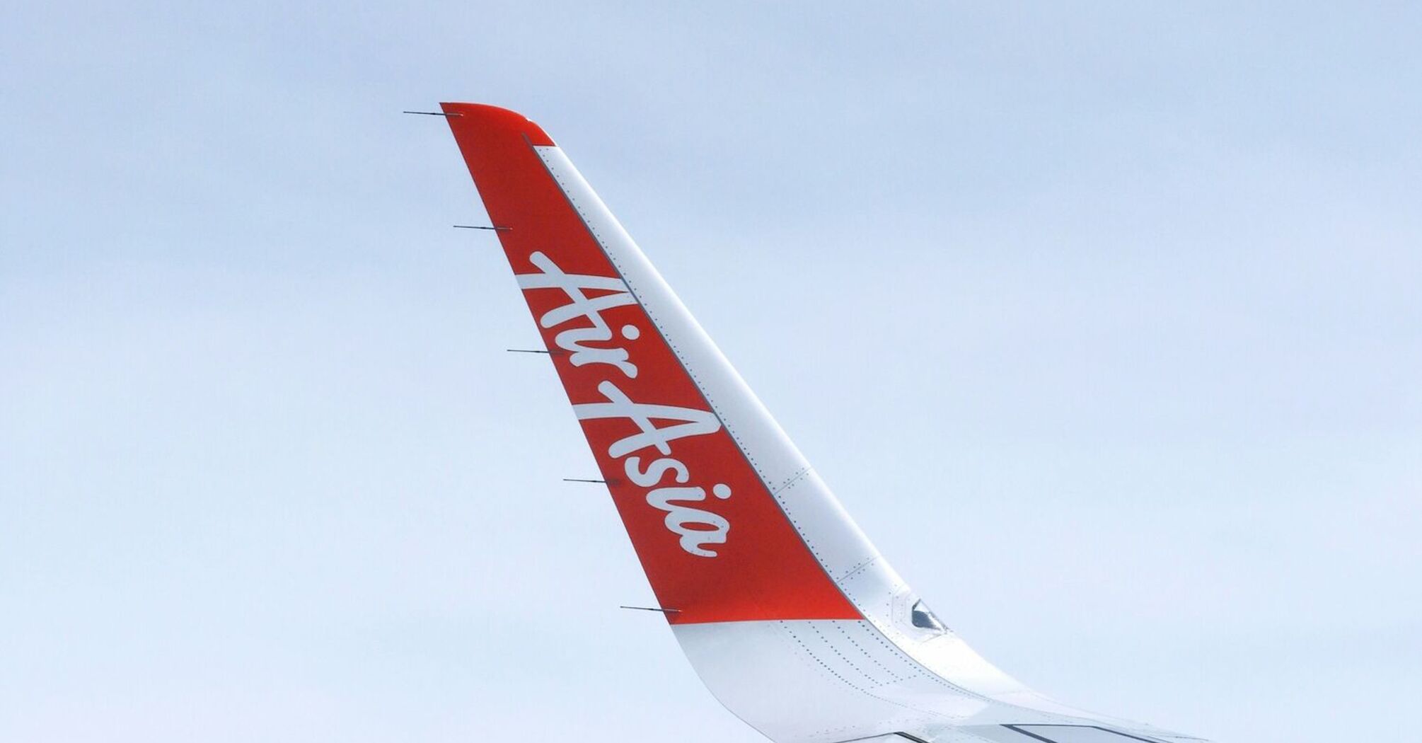 The wing of an AirAsia airplane against a clear sky, focusing on the wingtip with the AirAsia logo