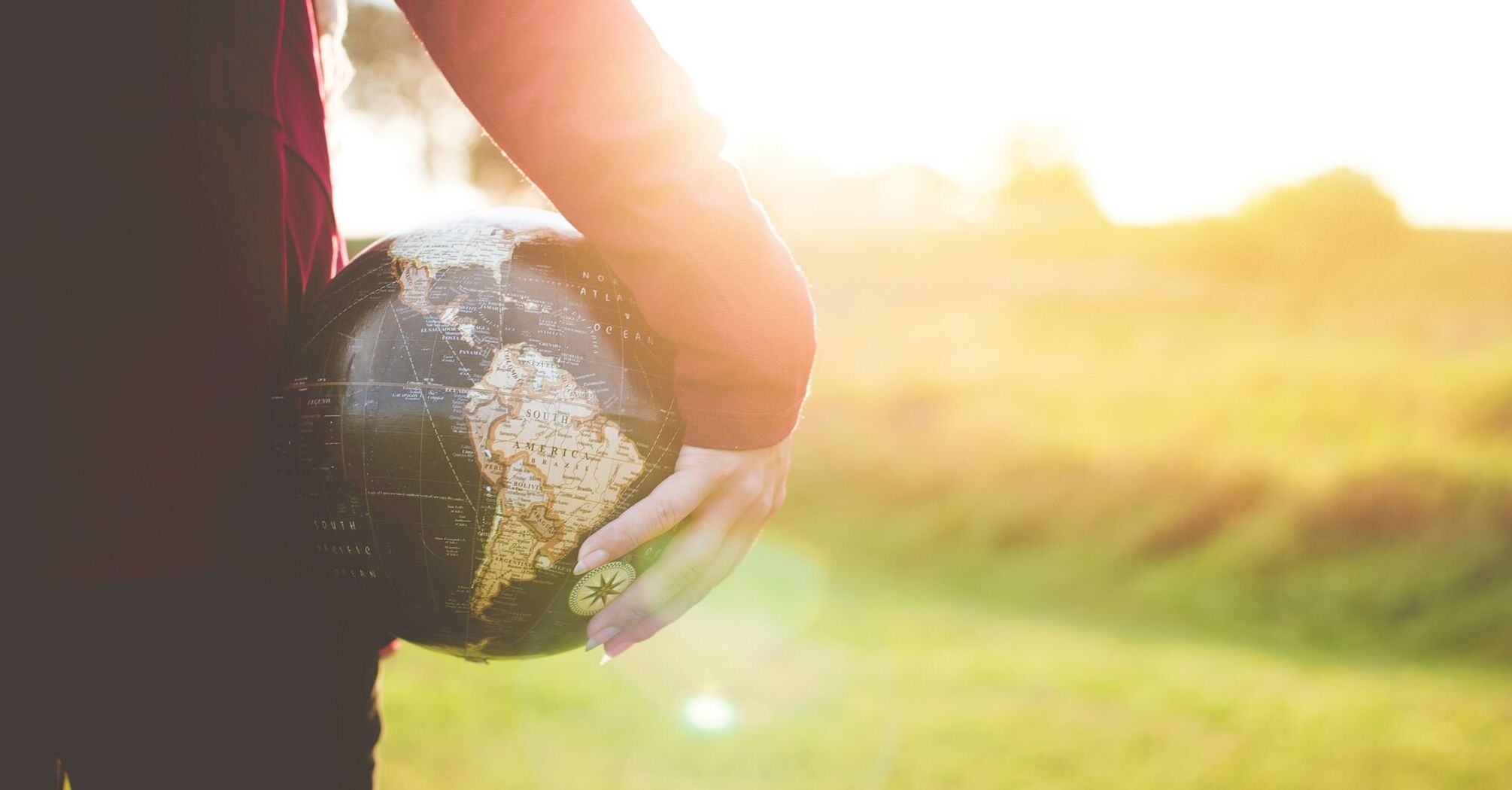 Person holding a small globe in sunlight, symbolizing global travel and exploration