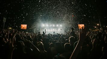 Crowd of people enjoying a concert with confetti falling from the sky at night, stage lights illuminating the scene