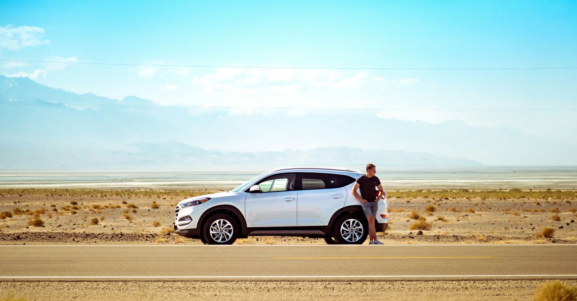 Man standing beside white suv near concrete road under blue sky at daytime
