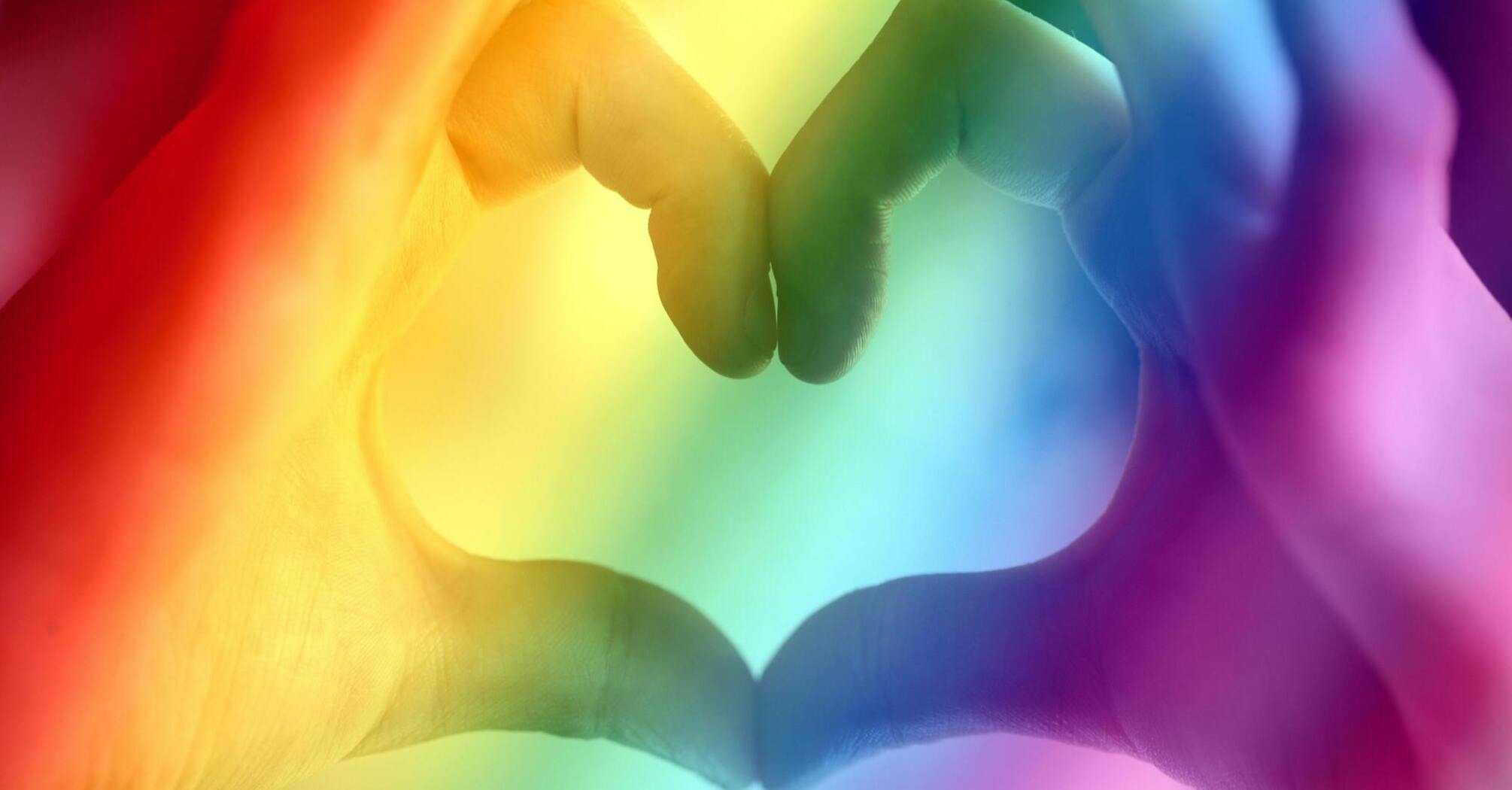 Two hands forming a heart shape against a vibrant rainbow background