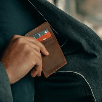 Person placing a brown leather wallet with credit cards into the pocket of a dark coat