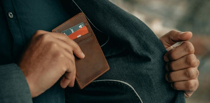 Person placing a brown leather wallet with credit cards into the pocket of a dark coat