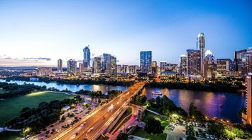 A panoramic view of Austin, Texas skyline at dusk with bright city lights and the Colorado River