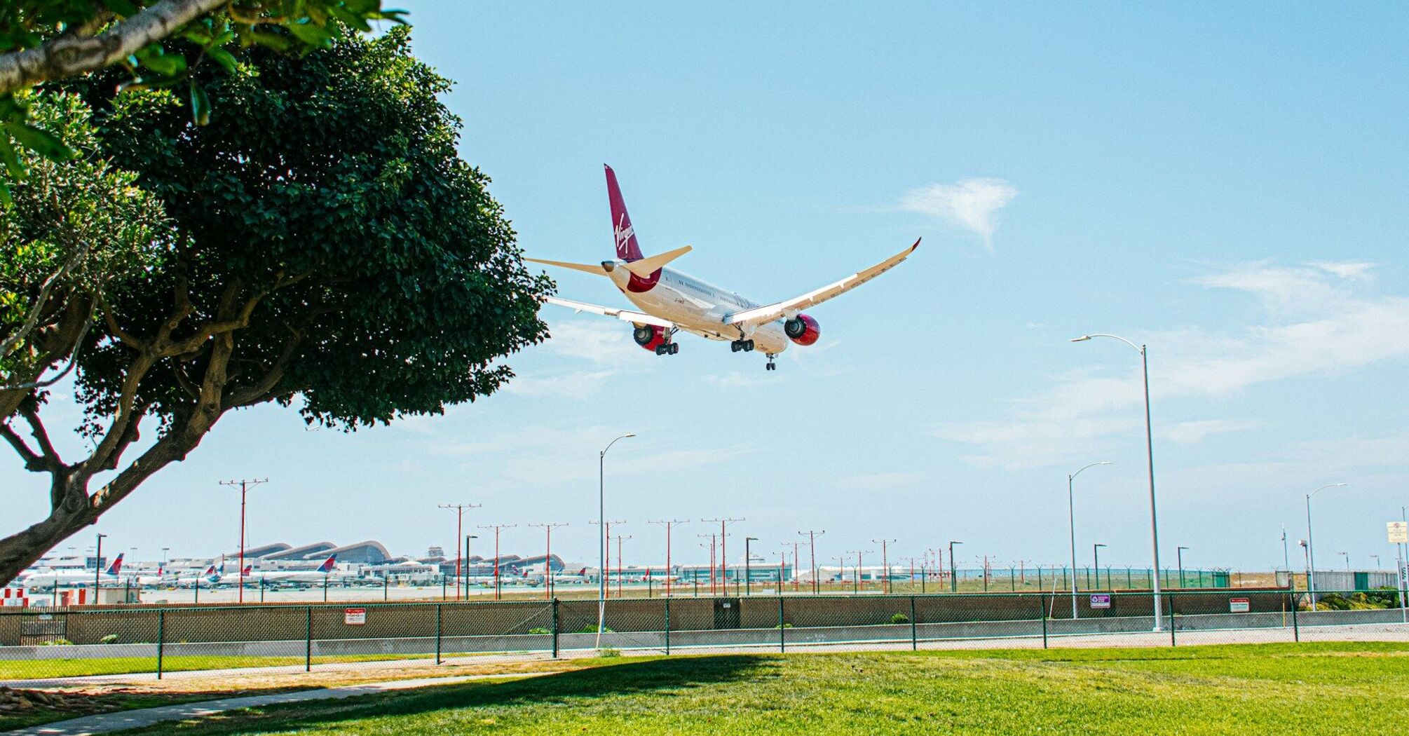 A commercial airplane approaching landing with its landing gear down near a lush green park
