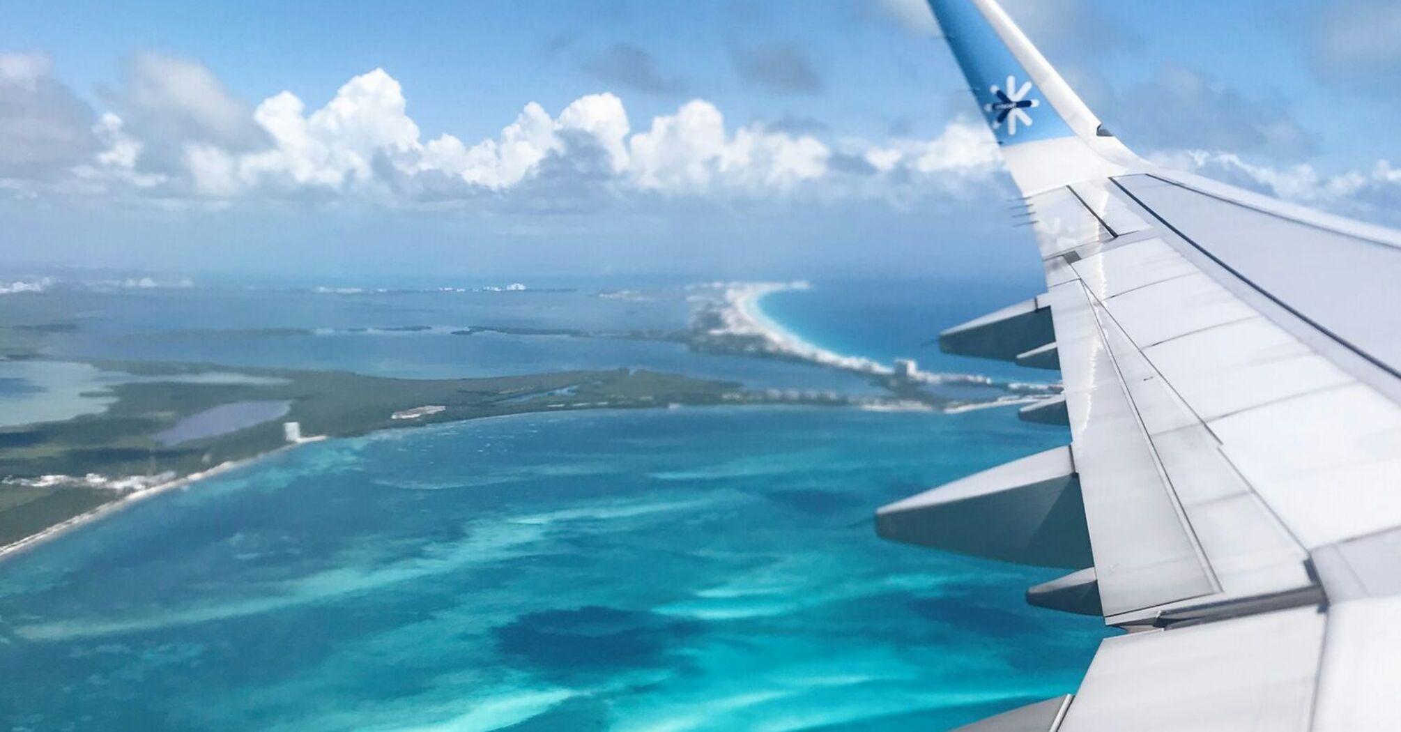 View of the crystal-clear turquoise waters of the Caribbean Sea from an airplane wing, with small islands near Cancún