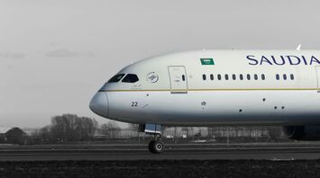 A Saudia Boeing 787 aircraft on the runway, side view, with a grayscale background highlighting the plane's livery
