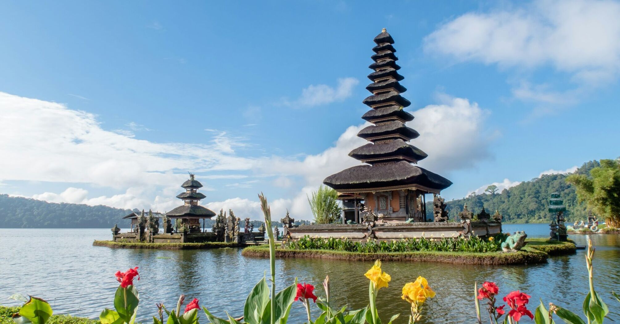A serene view of Pura Ulun Danu Bratan, a Hindu temple on Bratan Lake in Bali, with multi-tiered shrines, surrounded by lush greenery and blooming flowers 