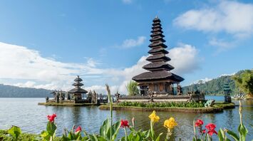 A serene view of Pura Ulun Danu Bratan, a Hindu temple on Bratan Lake in Bali, with multi-tiered shrines, surrounded by lush greenery and blooming flowers