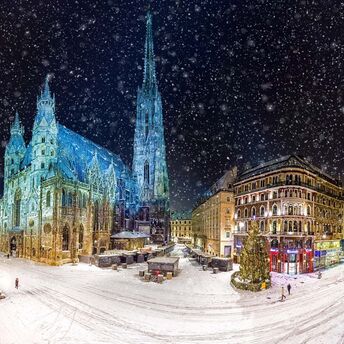 Snow-covered streets of Vienna at night with the illuminated St. Stephen's Cathedral and surrounding buildings