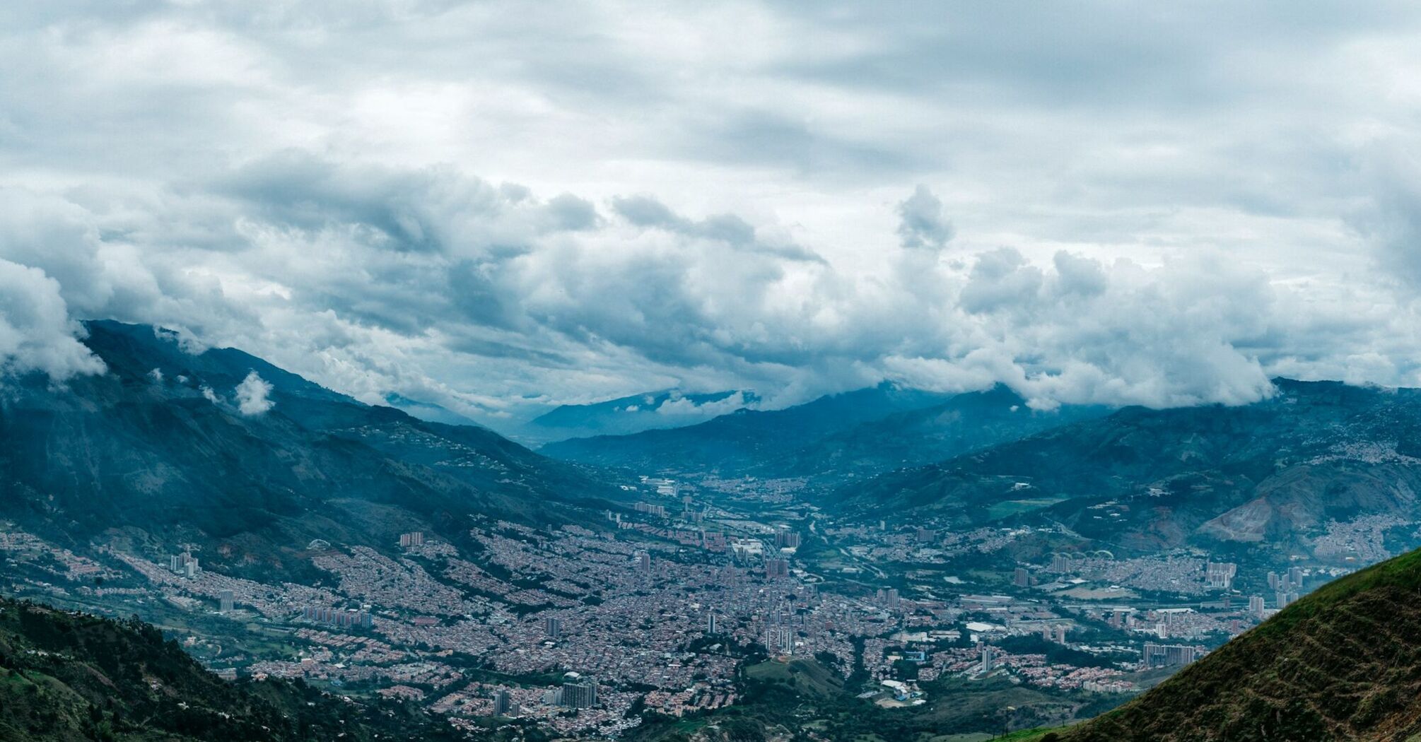 Aerial view of a city nestled in a valley with surrounding mountains and clouds overhead 