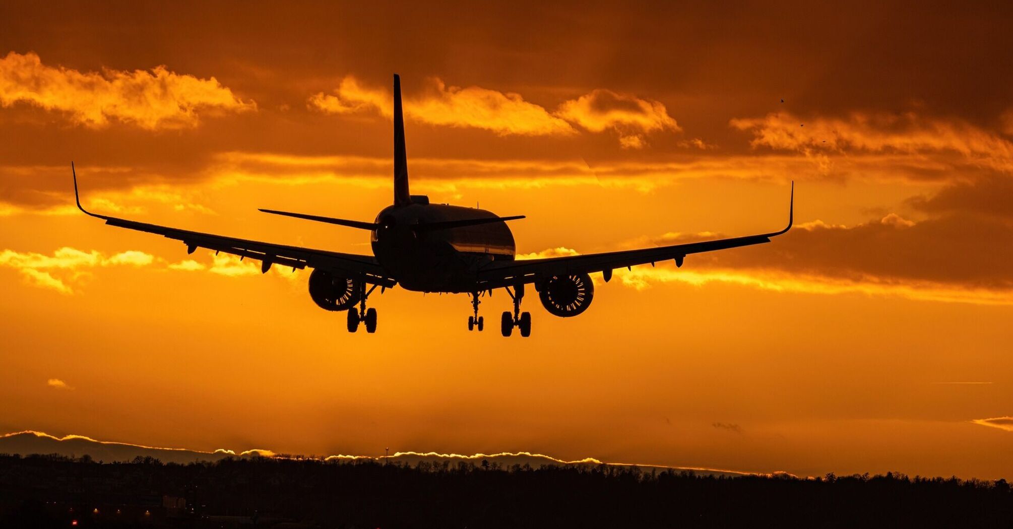 A silhouette of an airplane landing against a vibrant orange sunset sky
