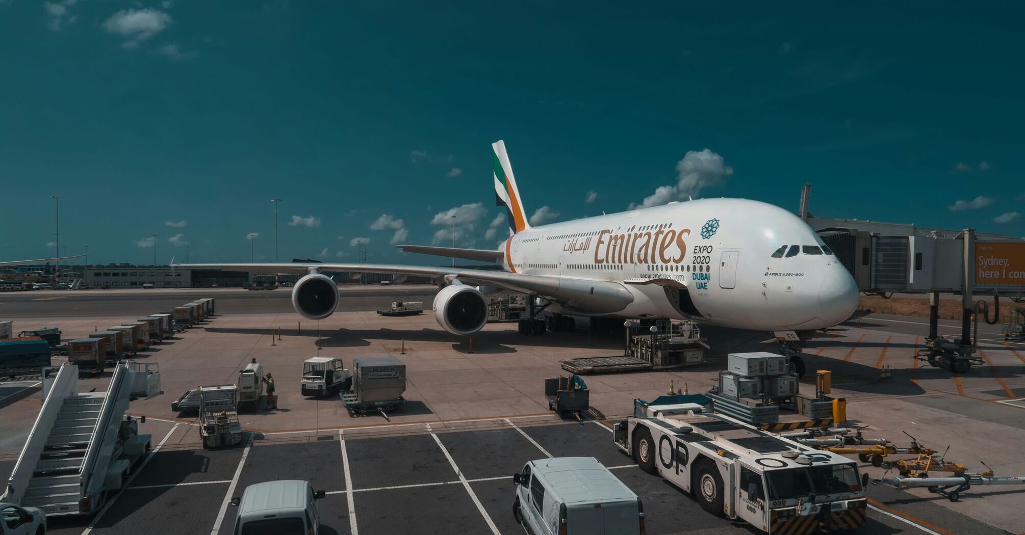 Emirates Airbus A380 parked at the gate with ground service vehicles around it