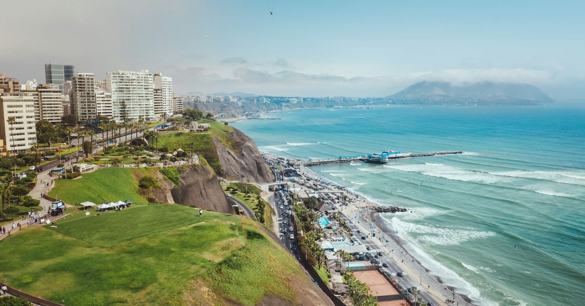 Aerial view of Lima, Peru, showcasing the coastline with a bustling beachfront, cliffs, and a modern cityscape in the background