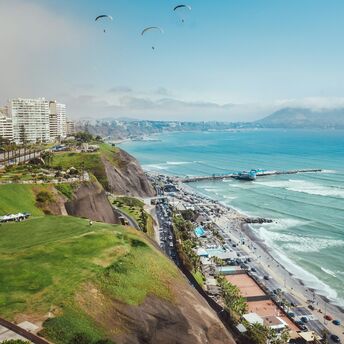Aerial view of Lima, Peru, showcasing the coastline with a bustling beachfront, cliffs, and a modern cityscape in the background