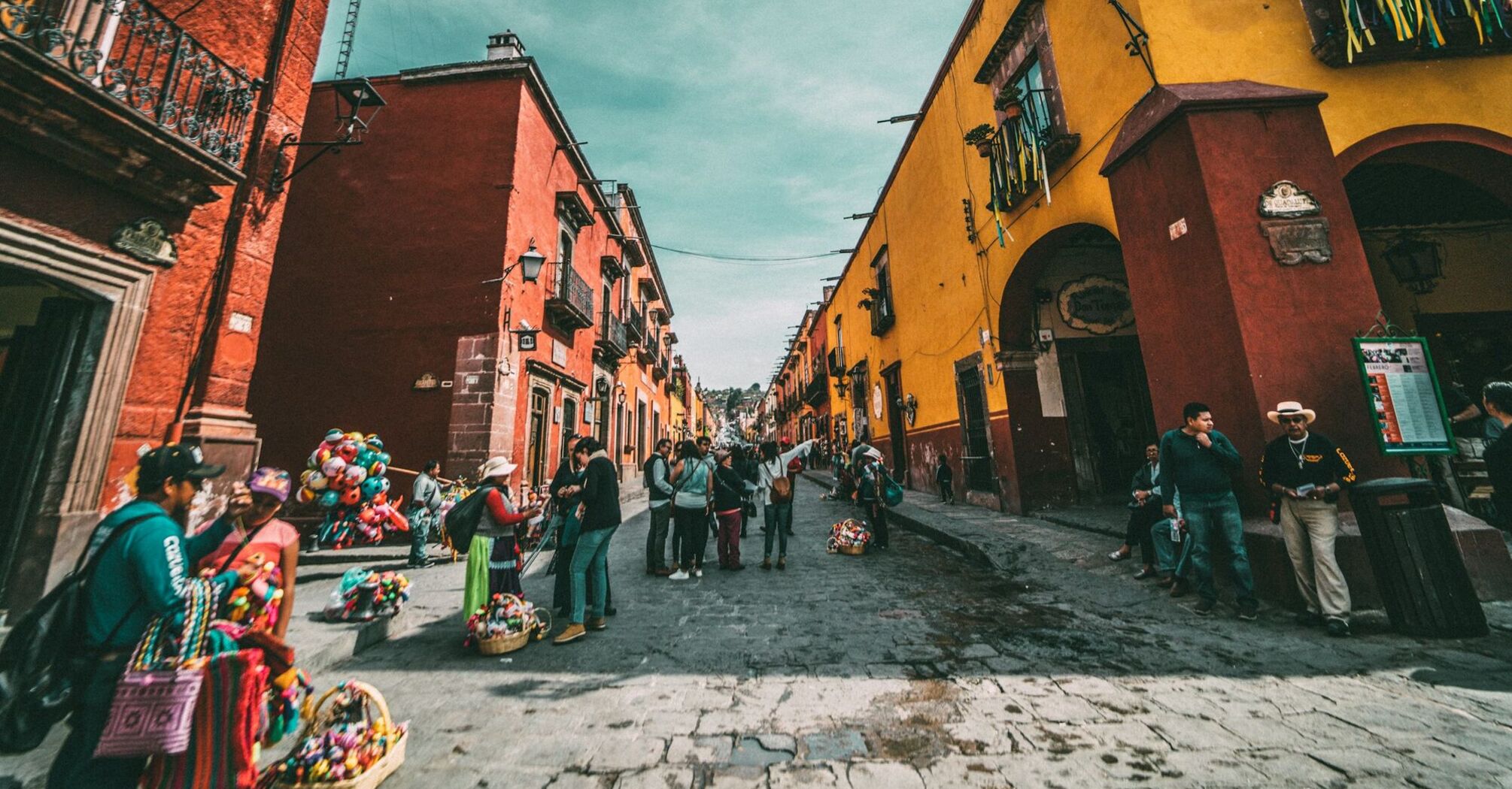 Colorful street scene in San Miguel de Allende, Mexico, with people walking and vendors selling traditional crafts 