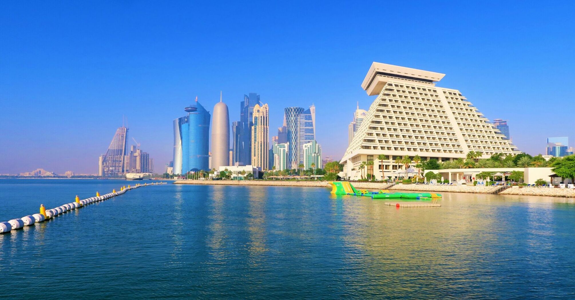 The skyline of Doha, Qatar, with modern skyscrapers along the coastline under a clear blue sky
