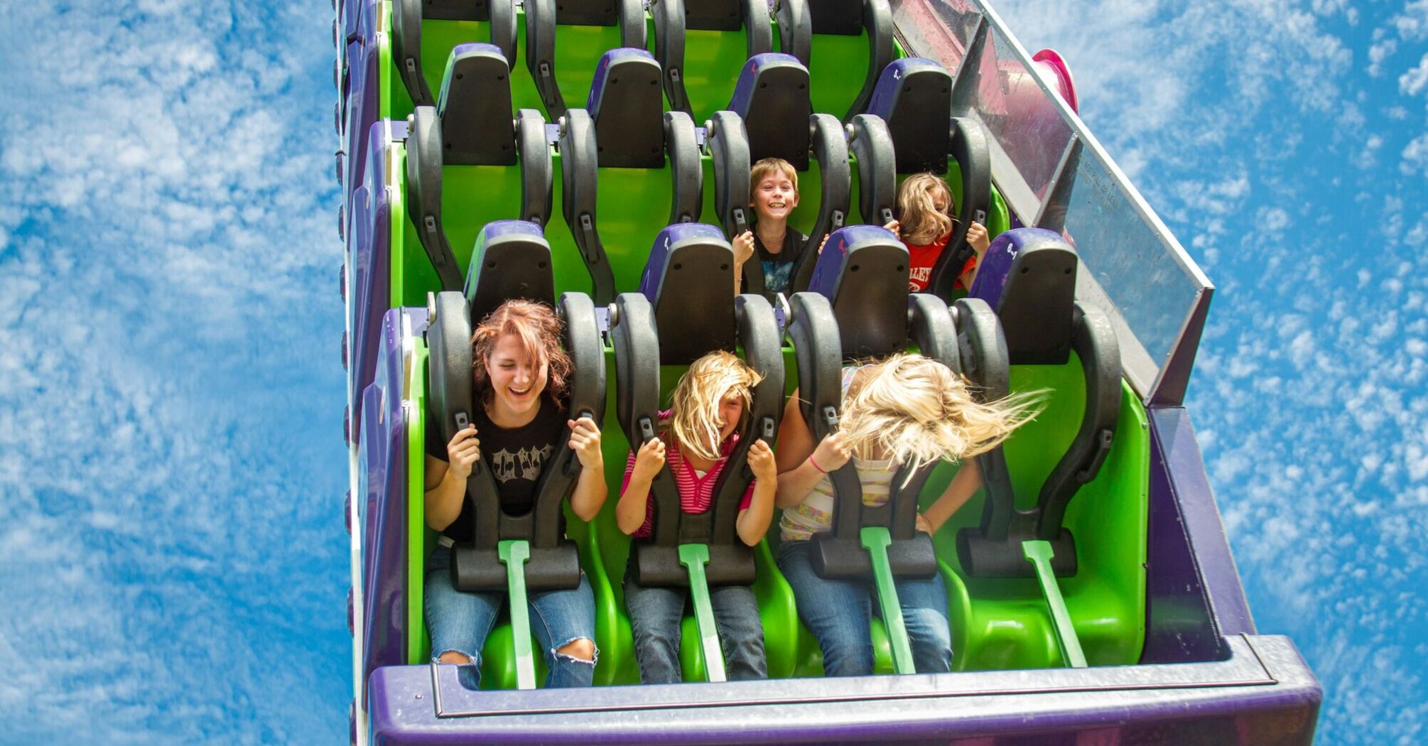People on a roller coaster ride, expressing excitement and joy against a clear blue sky