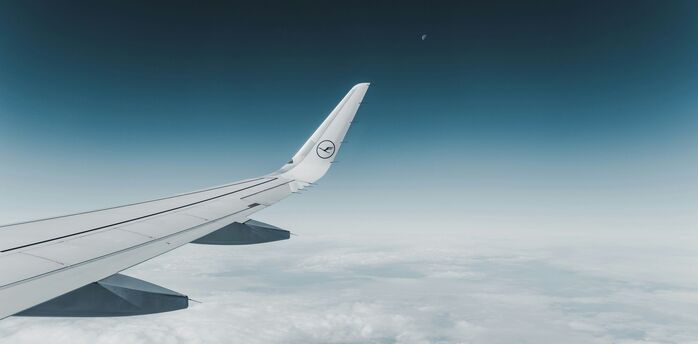 View of the airplane wing with Lufthansa logo flying high above the clouds with a clear blue sky and the moon in the background