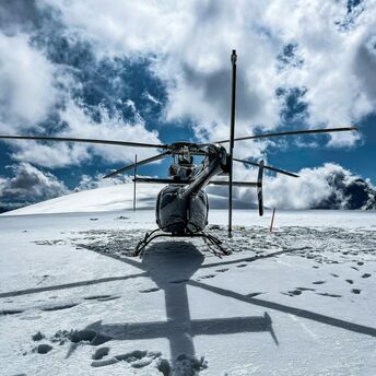 A helicopter parked on a snowy landscape with clouds in the blue sky above 