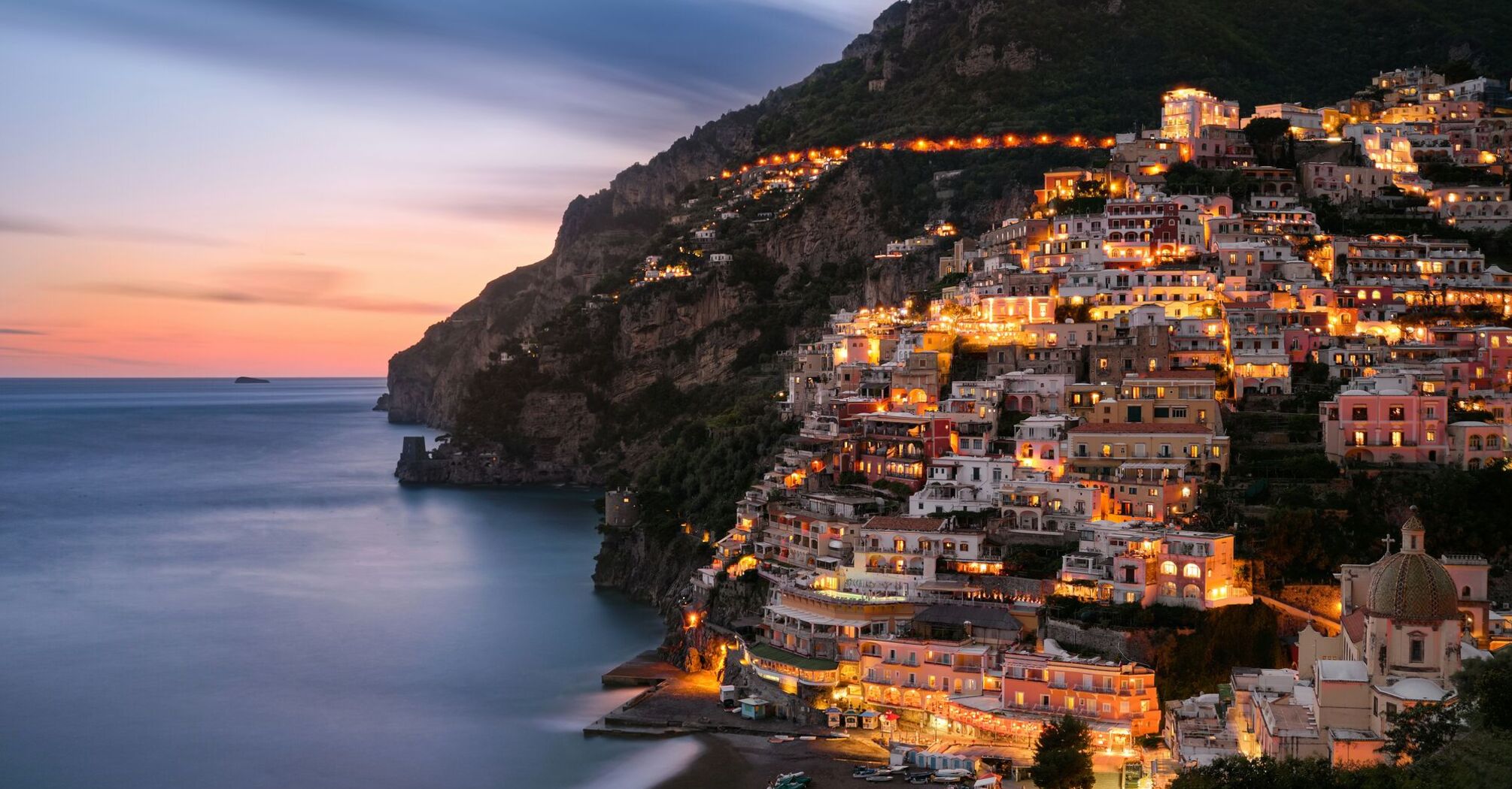 City buildings on mountain near body of water during eveningtime