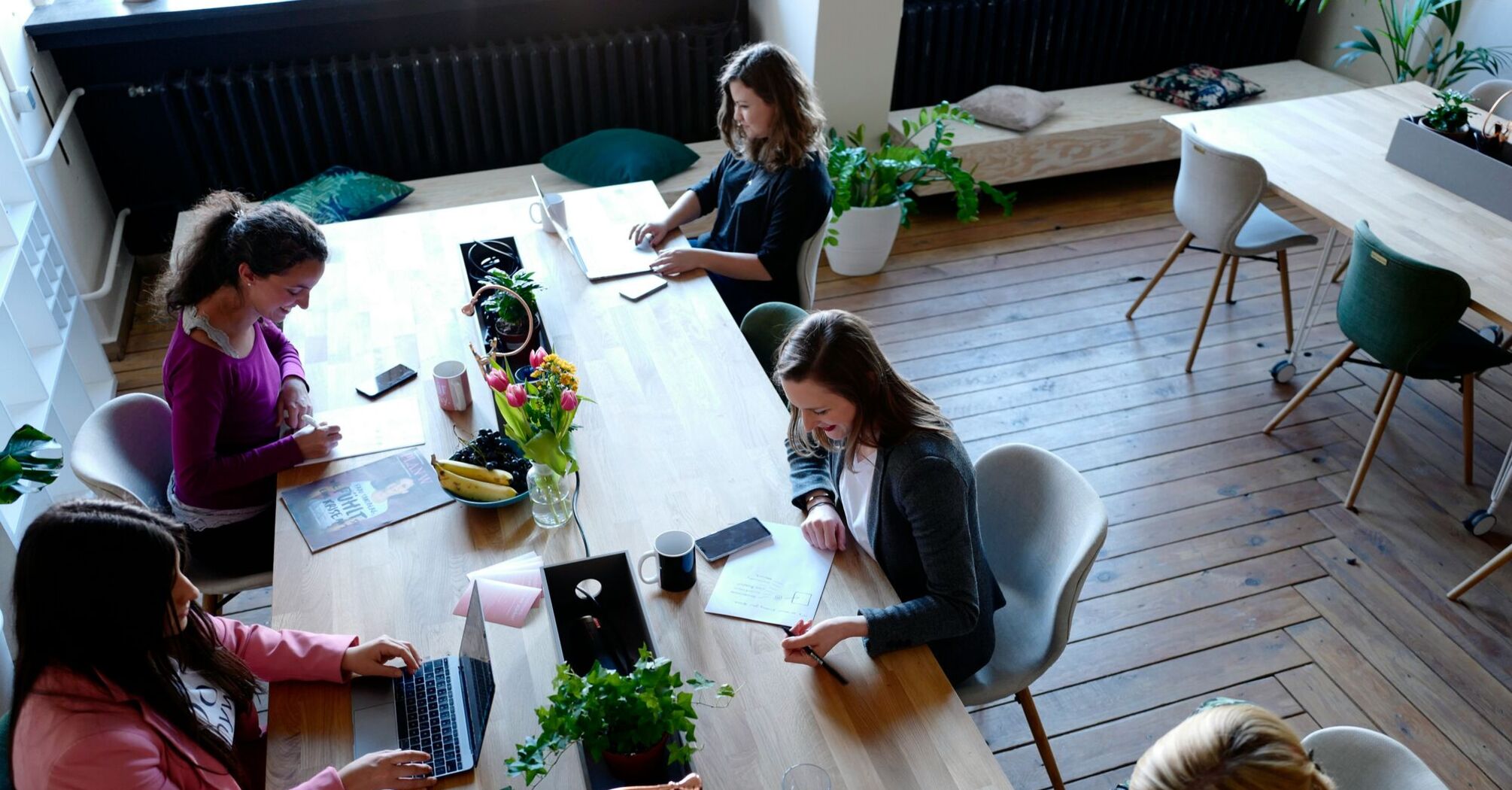 A group of women working together at a long table in a bright, modern co-working space