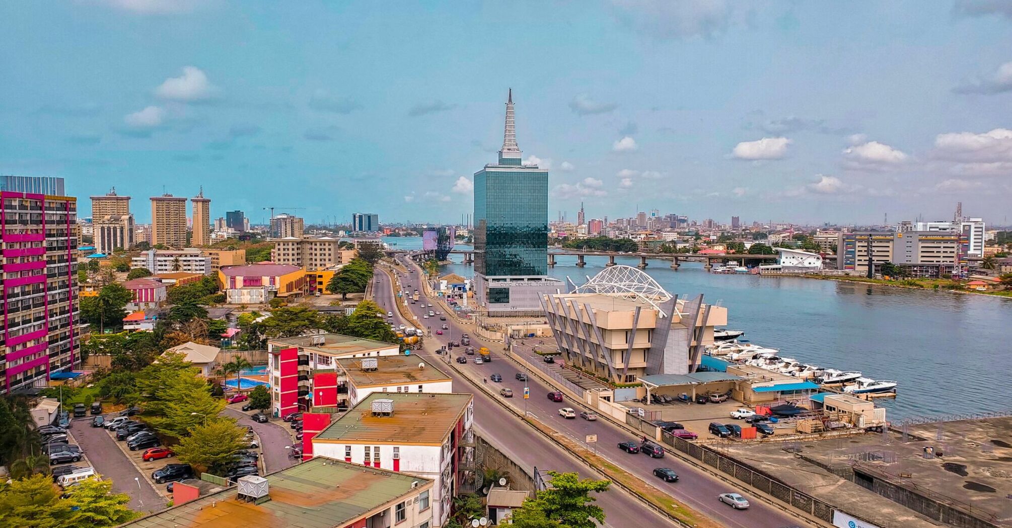 Aerial view of Lagos showcasing modern skyscrapers, bustling city streets, the calm Lagos Lagoon, and a clear blue sky