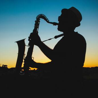 Silhouette of a saxophonist playing against an orange sunset sky