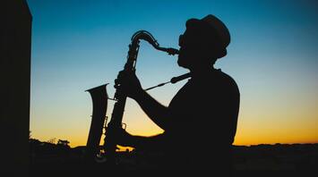 Silhouette of a saxophonist playing against an orange sunset sky