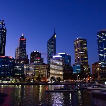 Twilight view of Perth's skyline reflecting on the water with illuminated office buildings and a sculpture by the esplanade