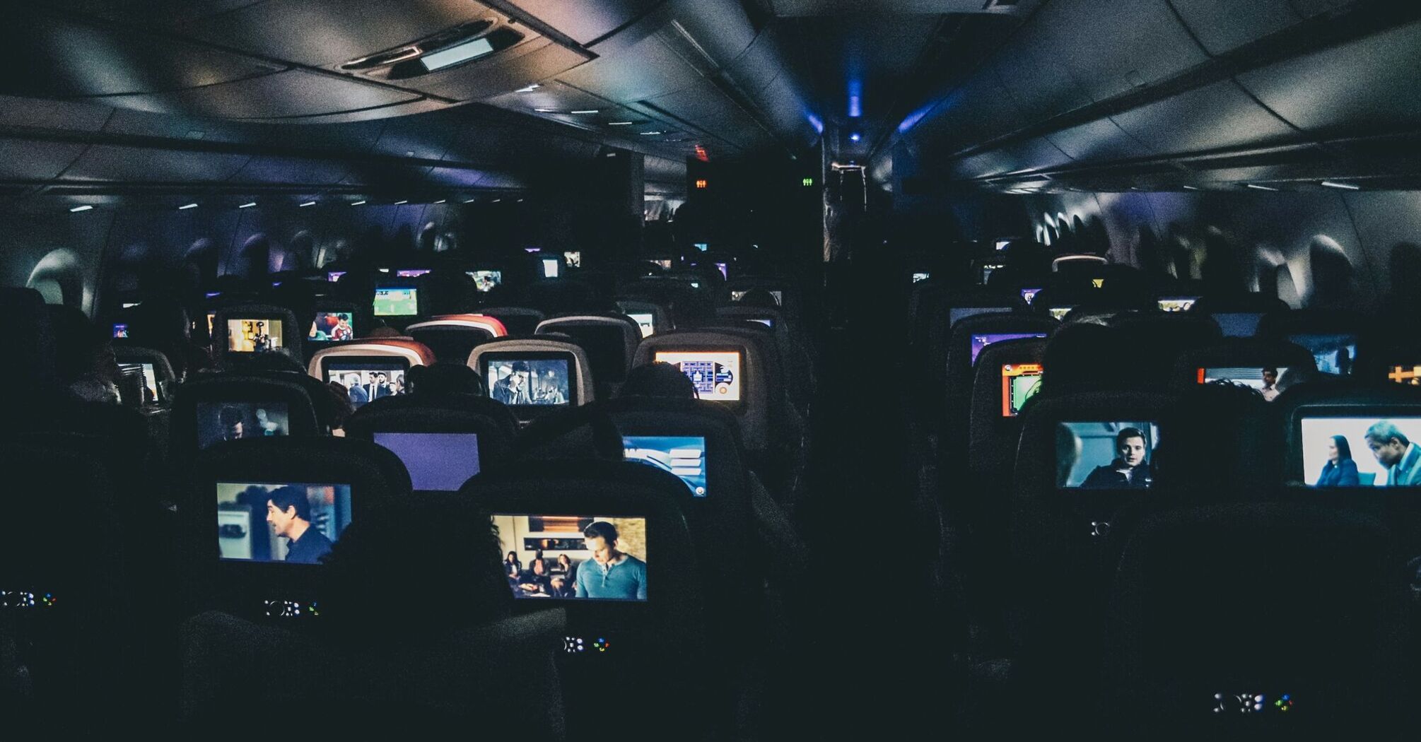 An airplane cabin at night with passengers watching various movies on individual seatback screens