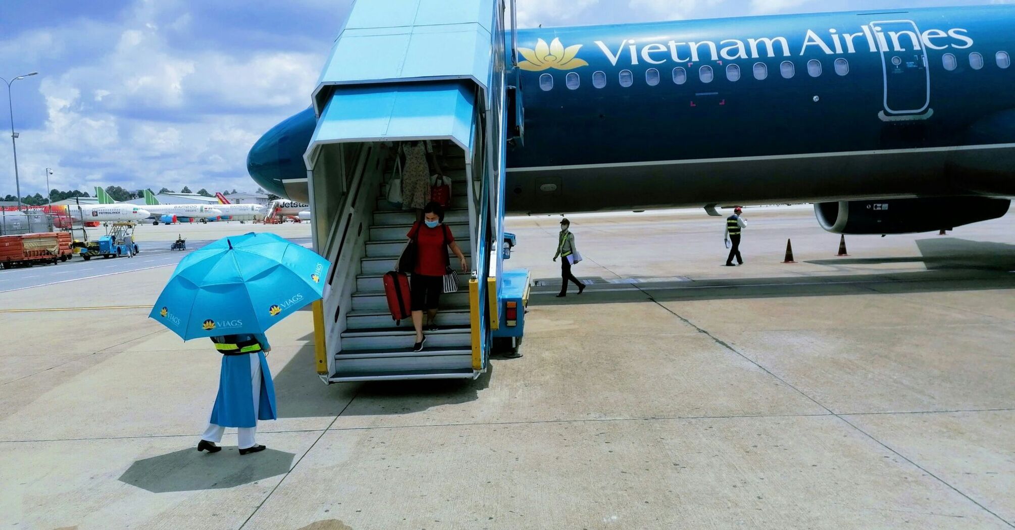 A passenger descending from a Vietnam Airlines aircraft with an attendant holding an umbrella at the foot of the stairway on the tarmac