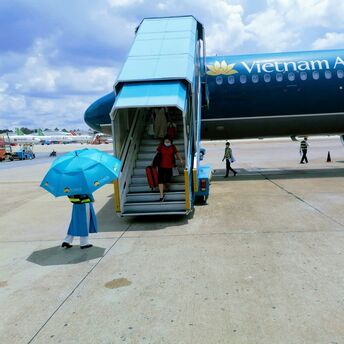 A passenger descending from a Vietnam Airlines aircraft with an attendant holding an umbrella at the foot of the stairway on the tarmac