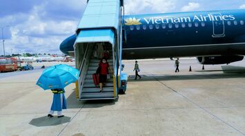 A passenger descending from a Vietnam Airlines aircraft with an attendant holding an umbrella at the foot of the stairway on the tarmac