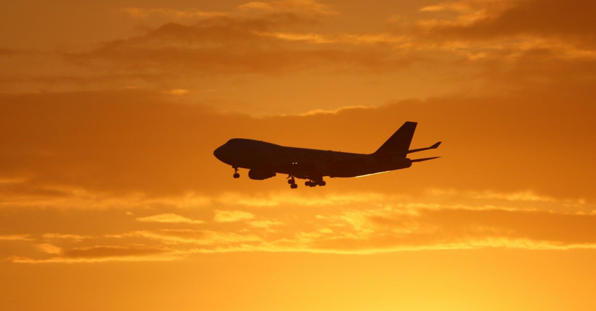 Silhouette of a cargo Boeing 747 airplane landing at sunset with a vibrant orange sky in the background 