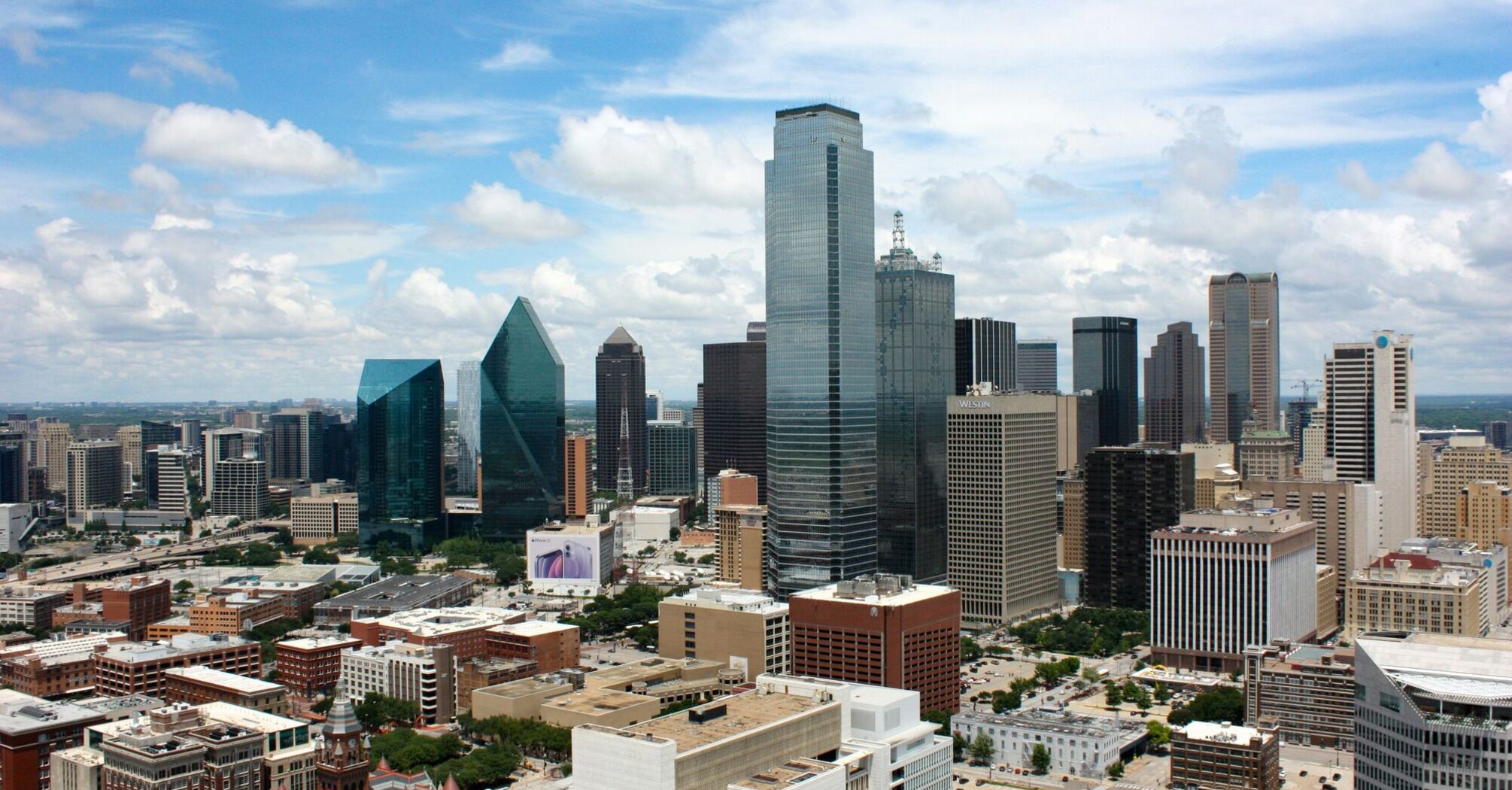 A daytime skyline view of Dallas, Texas, showcasing reflective skyscrapers, diverse architecture, and scattered clouds above