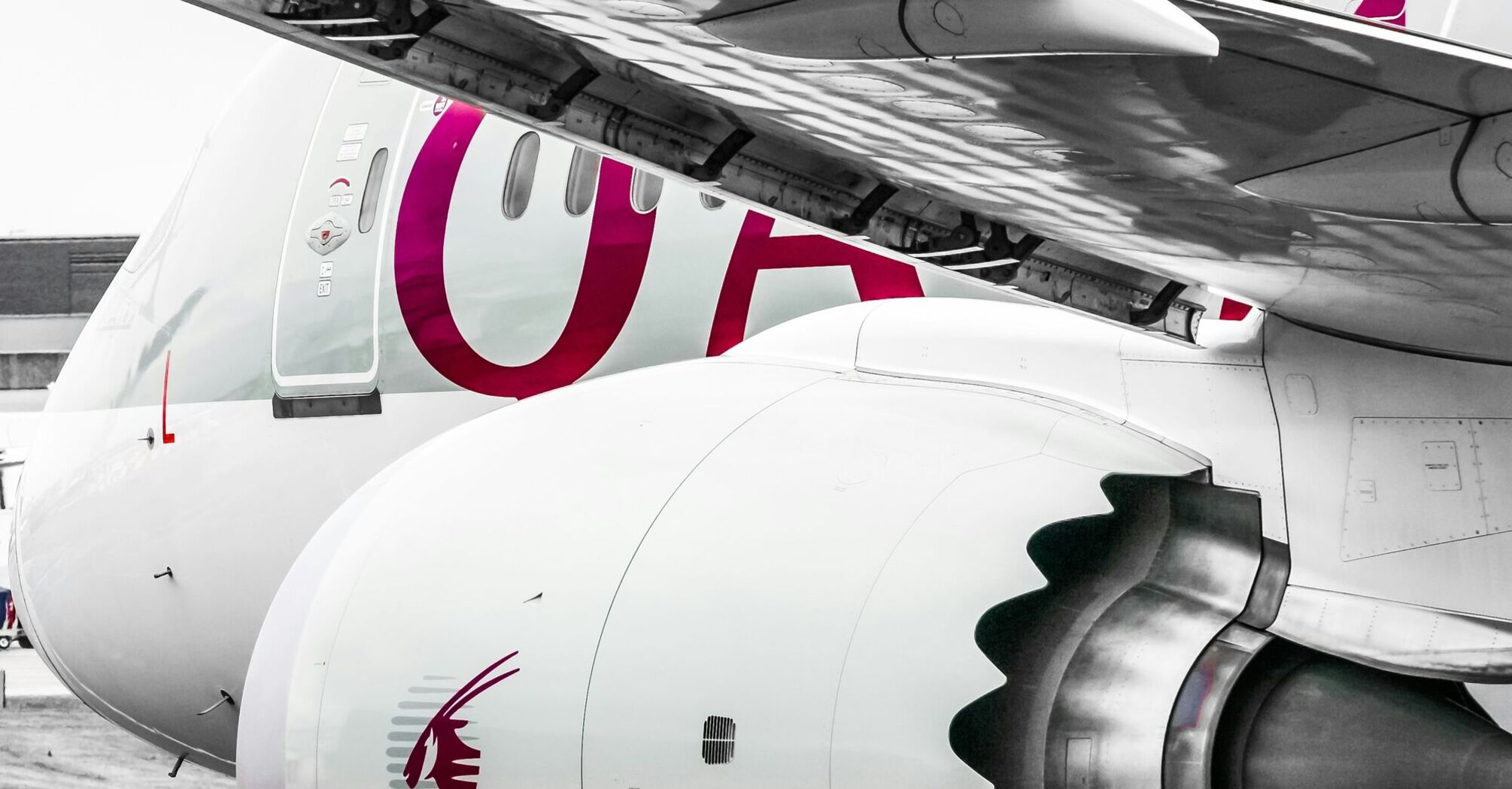 A close-up photograph of a white aircraft with the engine and part of the wing visible, adorned with the maroon logo of Qatar Airways