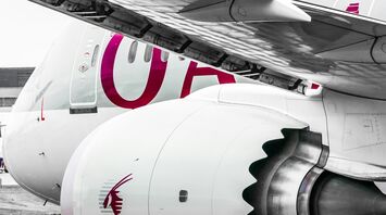 A close-up photograph of a white aircraft with the engine and part of the wing visible, adorned with the maroon logo of Qatar Airways