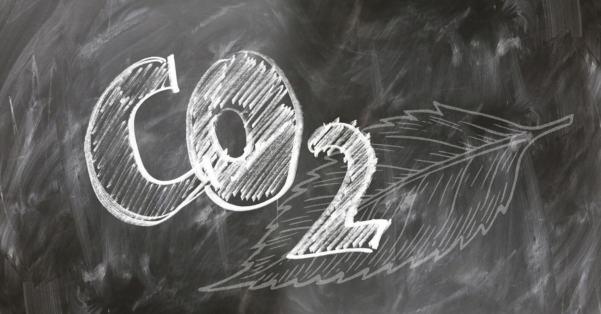 Chalk drawing of the 'CO2' chemical formula with an arrow on a blackboard, symbolizing the reduction or movement of carbon emissions