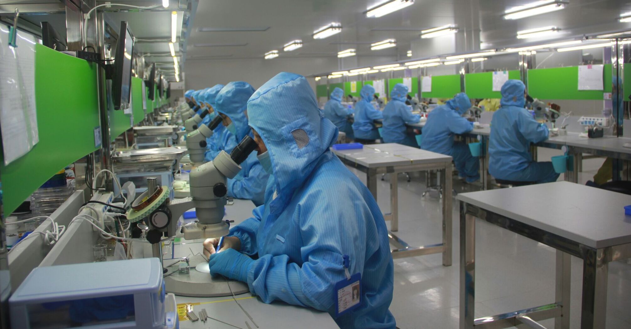 Workers in blue protective suits operating microscopes and equipment in a clean, brightly lit laboratory 