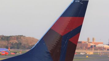 The tail fin of a Delta Airlines aircraft with the company's distinctive red, white, and blue logo, parked on the tarmac