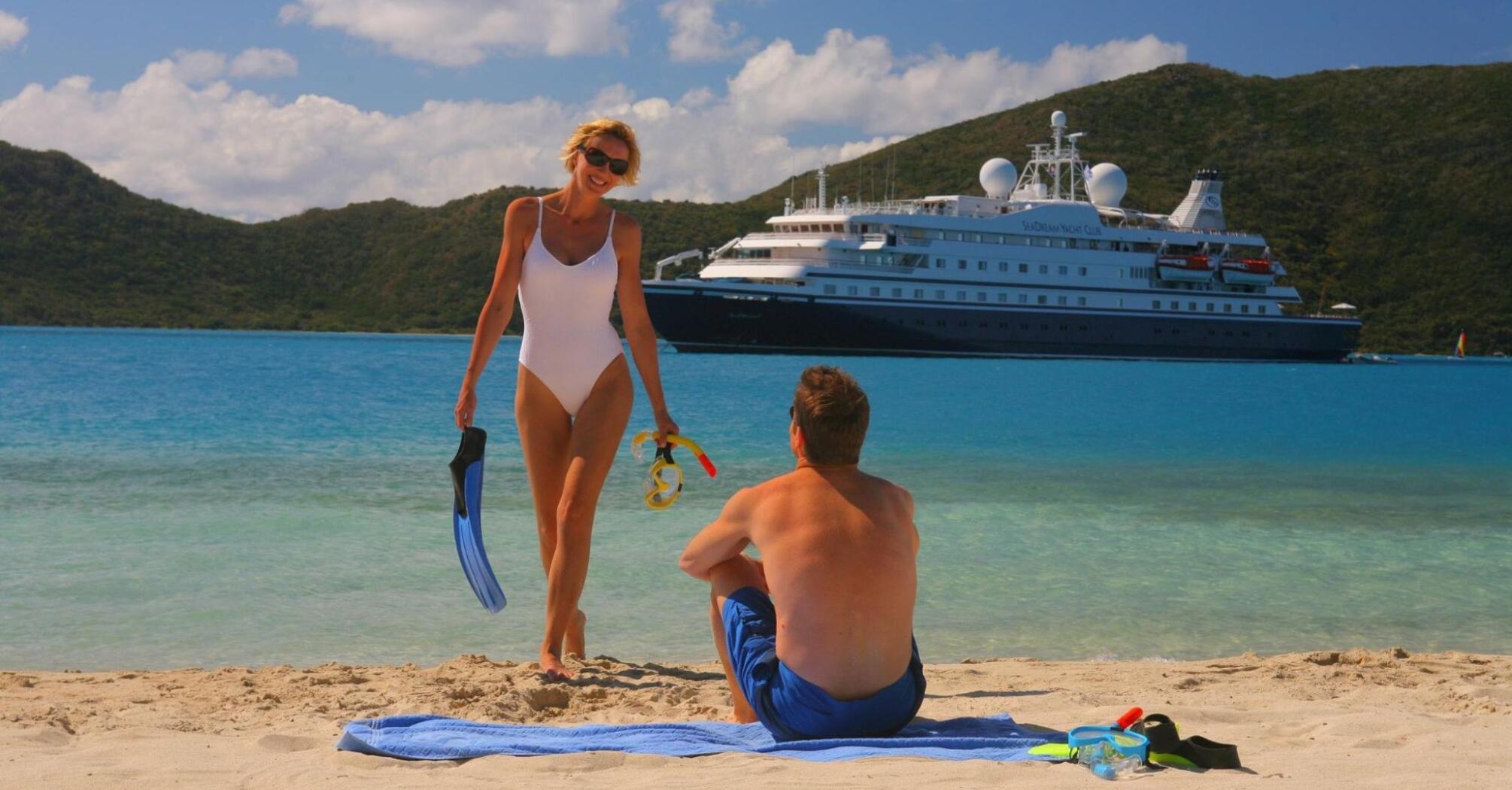A married couple relaxes on the shore with a cruise ship in the background