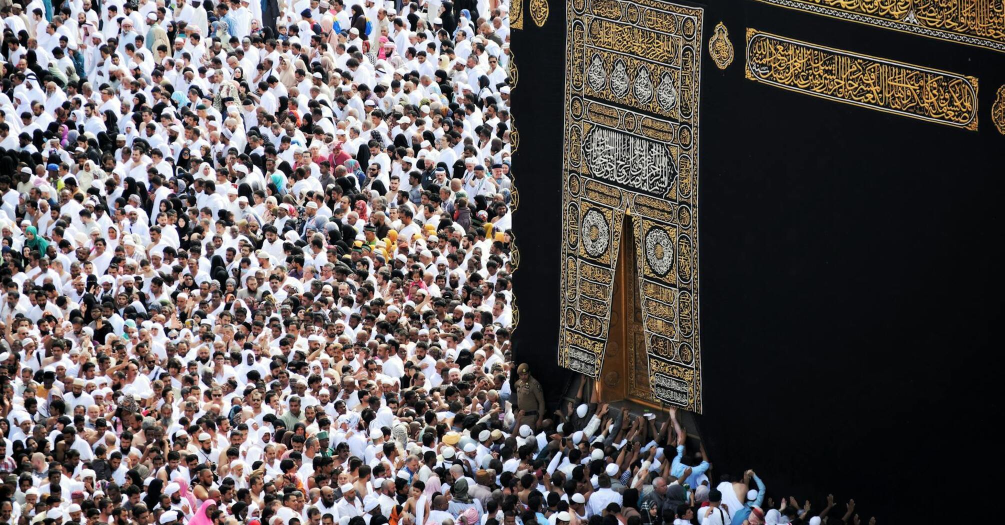 A large crowd of people dressed in white Ihram clothing performing the Islamic pilgrimage, Hajj, around the Kaaba in Mecca